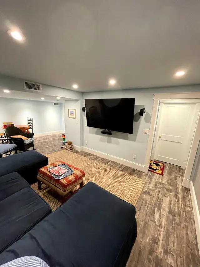 Finished basement family room with gray sectional, wall-mounted TV and recessed lighting