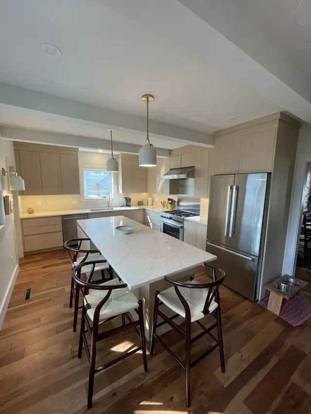 Kitchen remodel with light wood cabinets, marble-look island table, gold pendant and stainless refrigerator