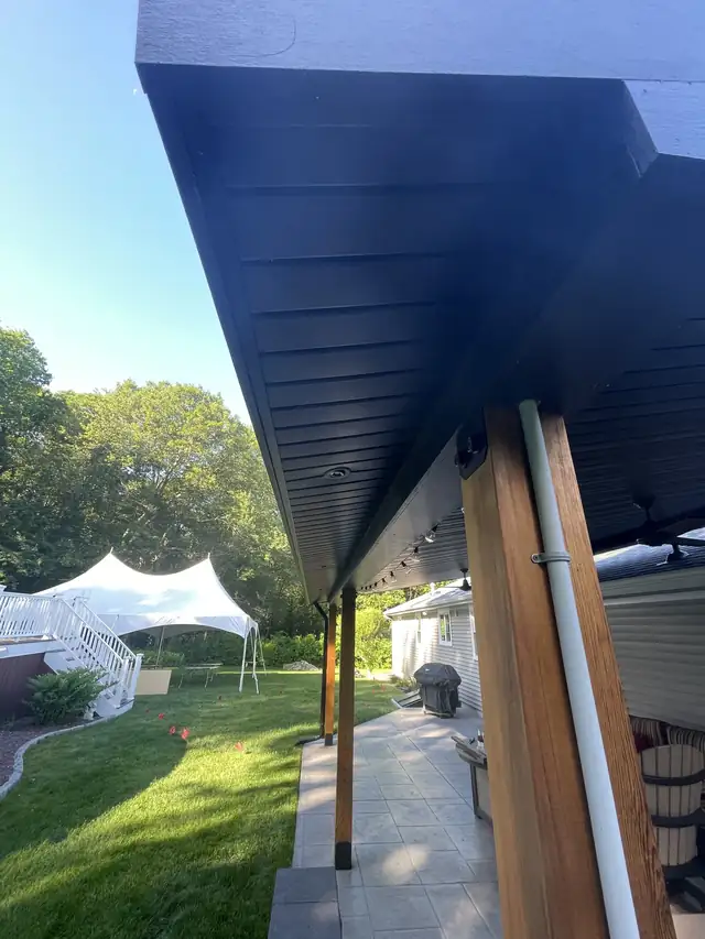 Covered patio pavilion with navy ceiling, wood posts and paver patio beside a gray-sided home