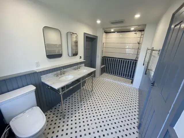 Bathroom with a marble console sink, two mirrors, gray beadboard wainscot and black and white mosaic floor tile