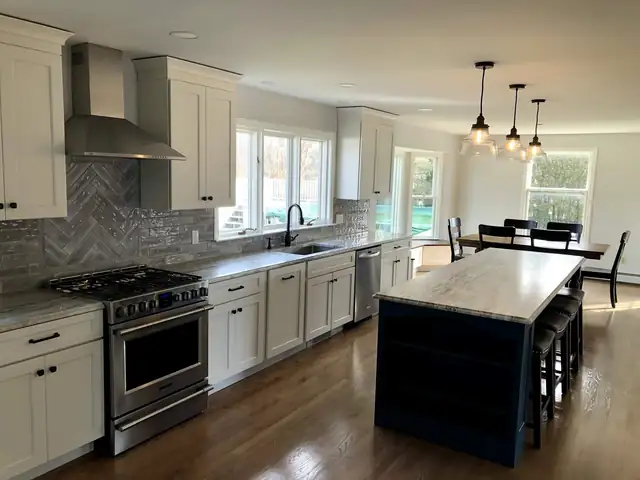 Kitchen remodel in Swansea, MA with white shaker cabinets, a navy island with stone top, herringbone backsplash and stainless range hood