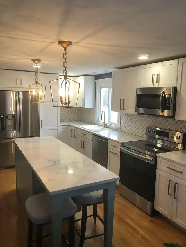 Kitchen remodel in Warren, RI with white cabinets, a gray island with marble-look top and lantern pendants